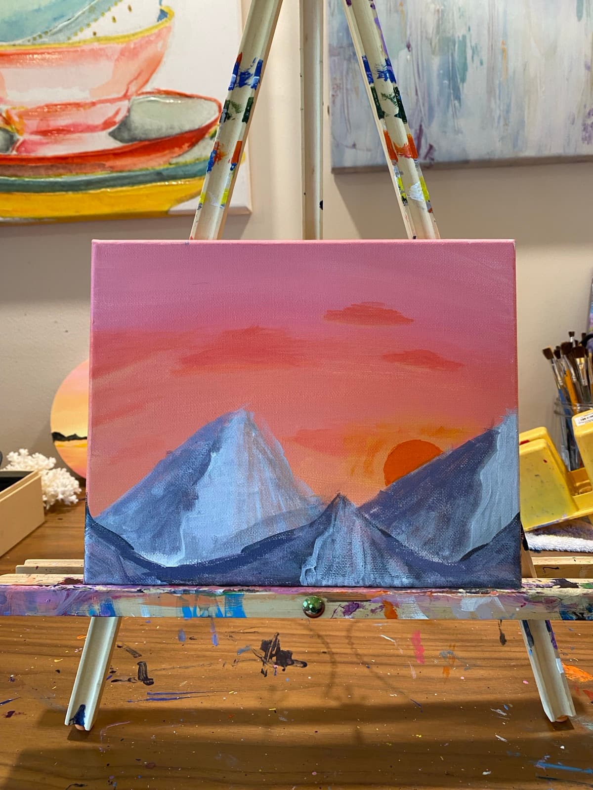 Mouth painting: coral and orange sunset over blue and silver mountain peaks.