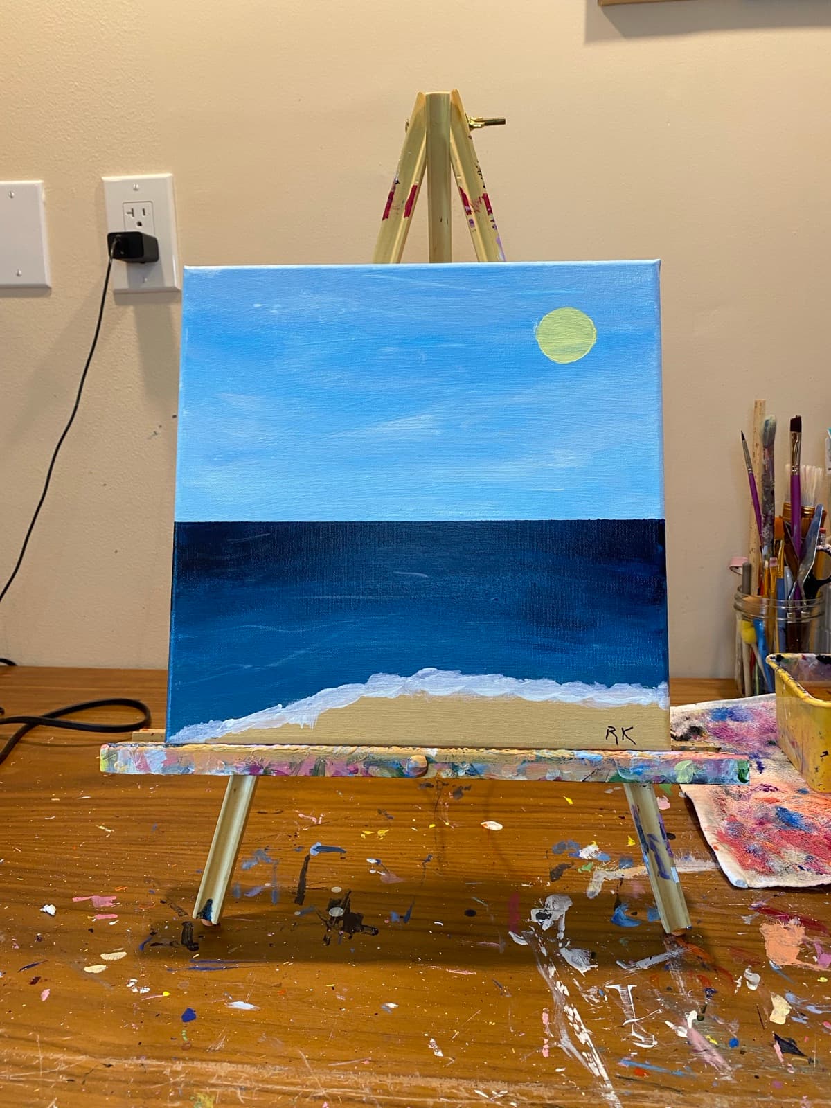 Mouth painting: a full yellow moon over a deep blue ocean and pale shore.